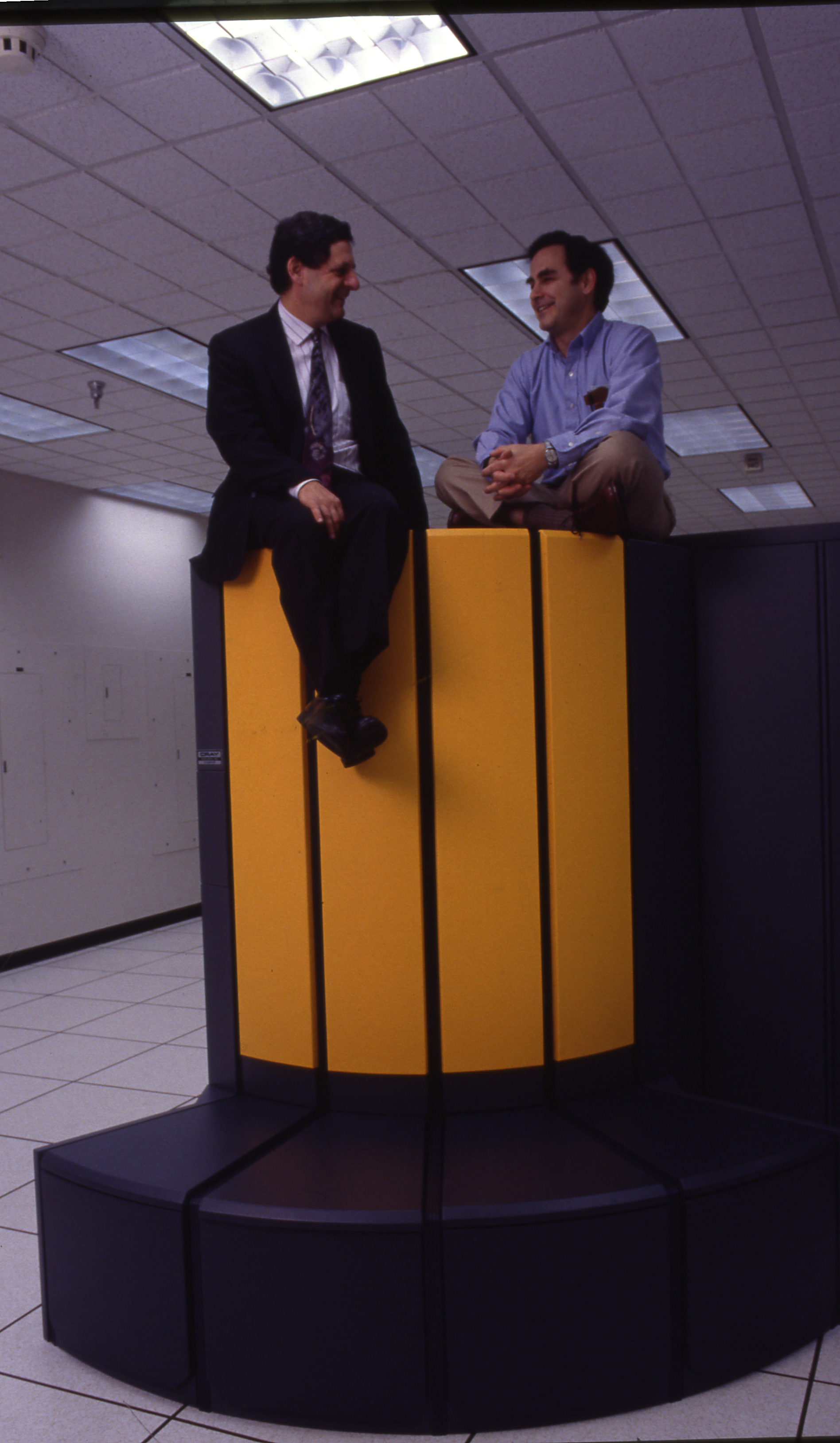 Two met sit atop a black and yellow supercomputer component.