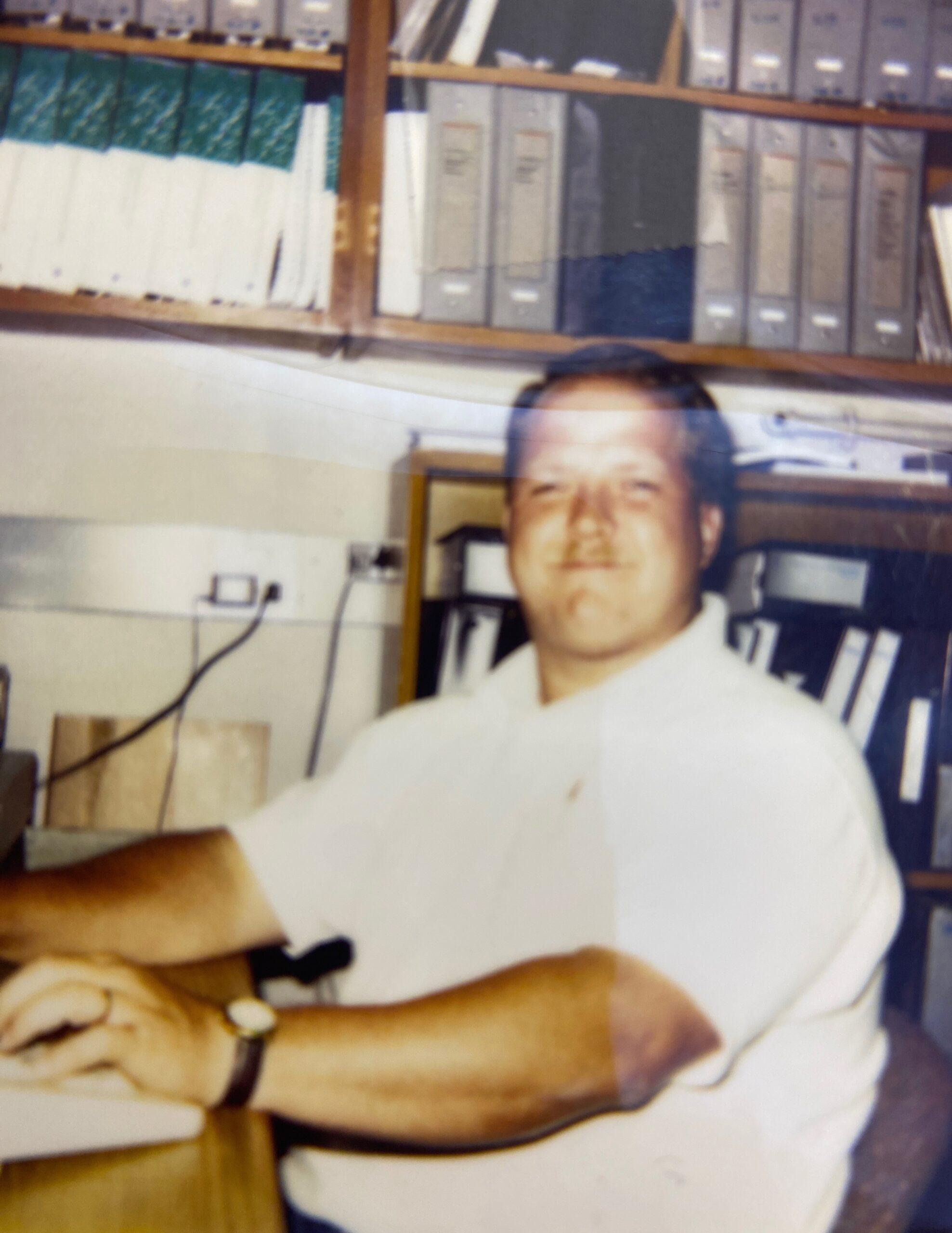 Photograph of Ken at a desk with binders and papers.