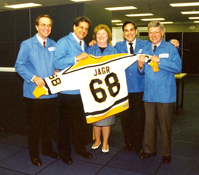 Five people in lab coats smile while holding a hockey jersey that says the name 