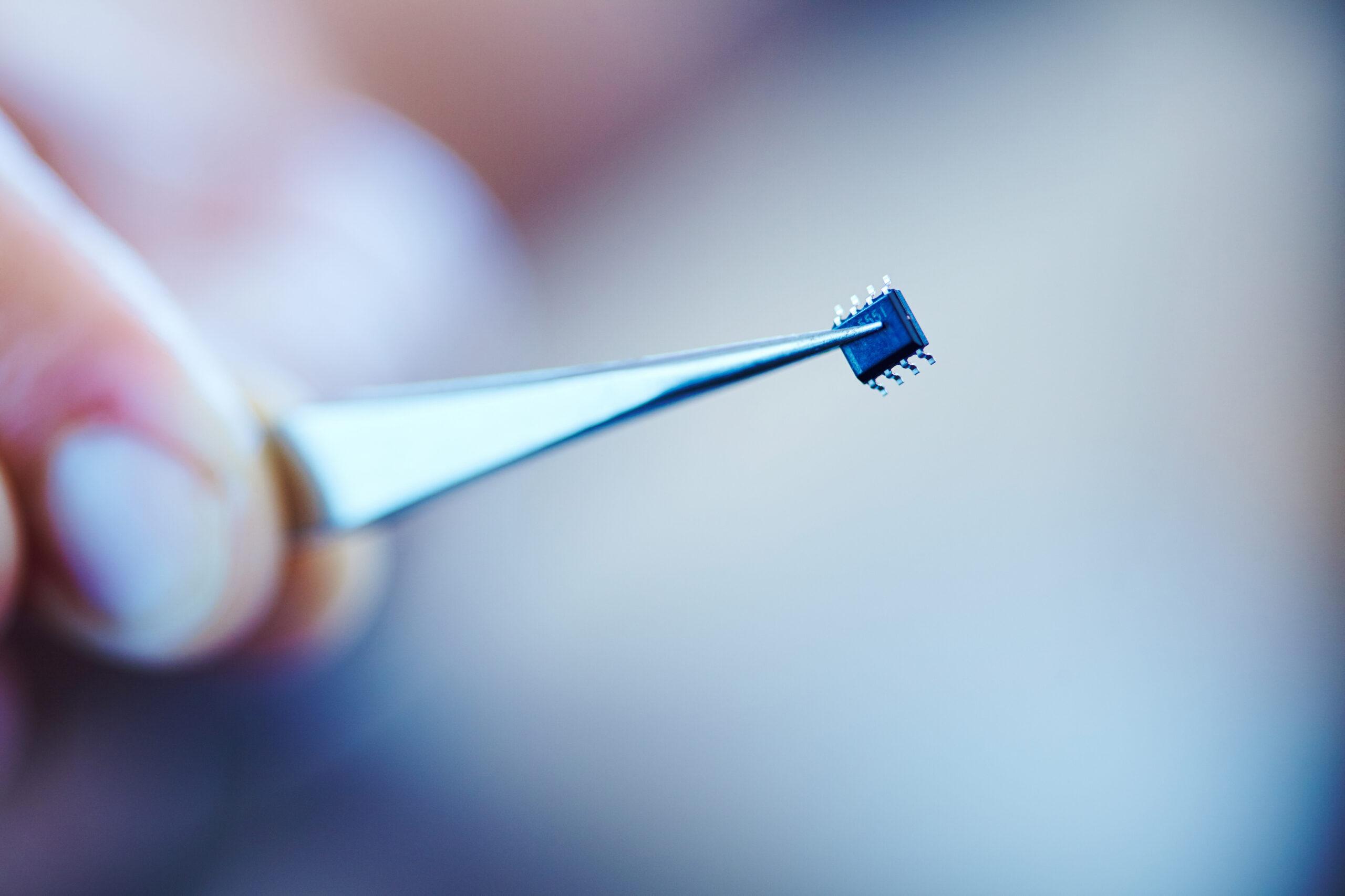 A microchip held with a pair of  tweezers
