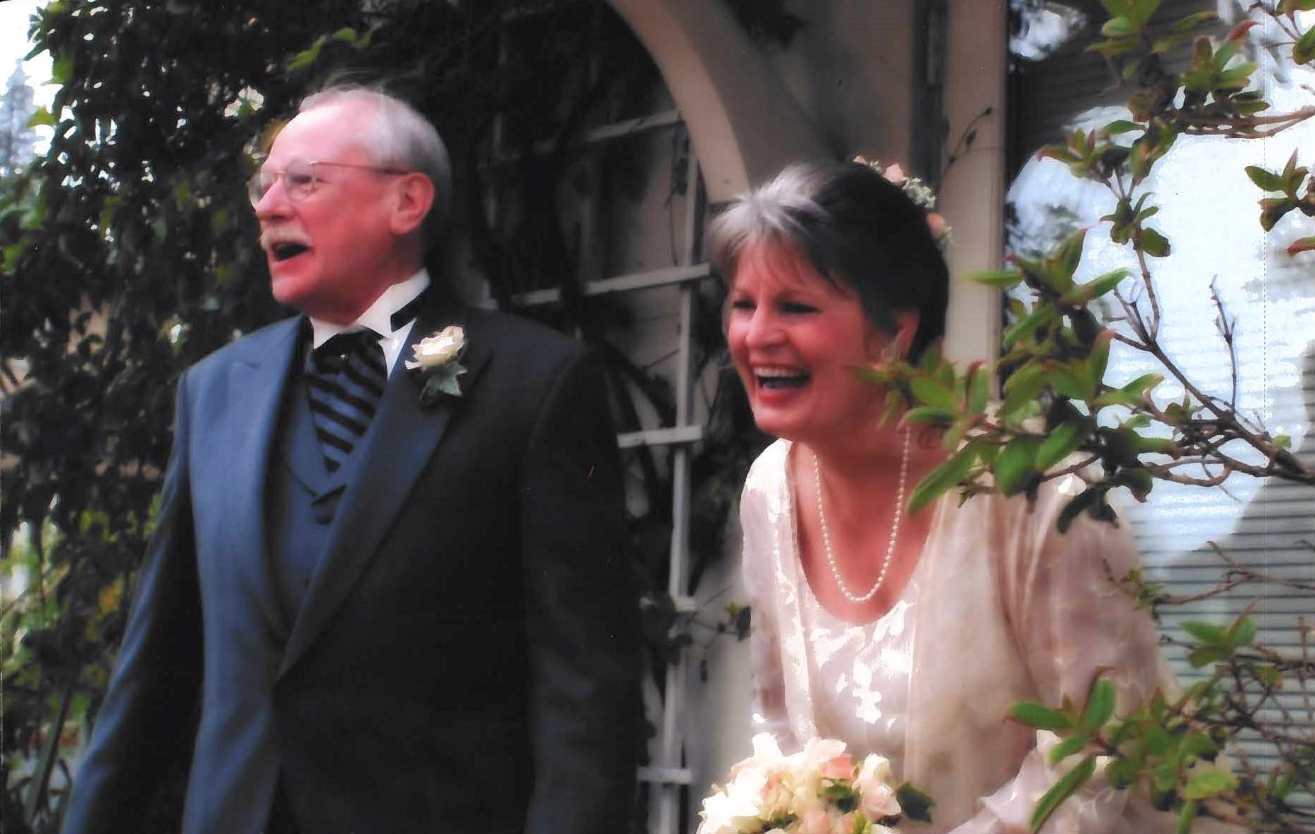 A man and a woman laugh and smile in wedding attire. 