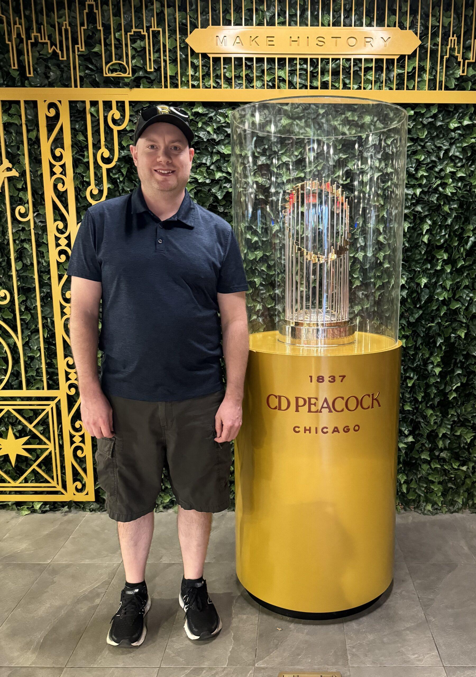 A man stands next to the Chicago World Series trophy.